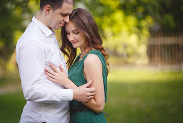 Young man and woman couple in a blooming apple garden. Tender holding each other. Spring lovestory. Brown-haired girl with long hairs. Young family
