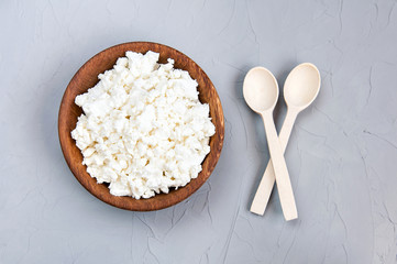 Homemade cottage cheese, curd in a wooden bowl on a grey rustic background. Healthy food. Top view, free space.