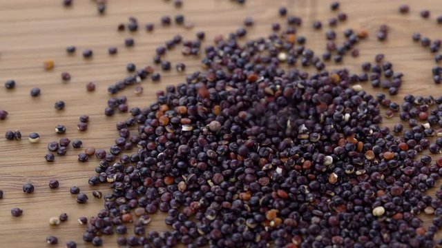 Gluten free black quinoa grain, falling on wood surface