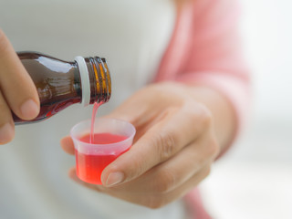 healthcare, people and medicine concept - woman pouring medication or antipyretic syrup from bottle...