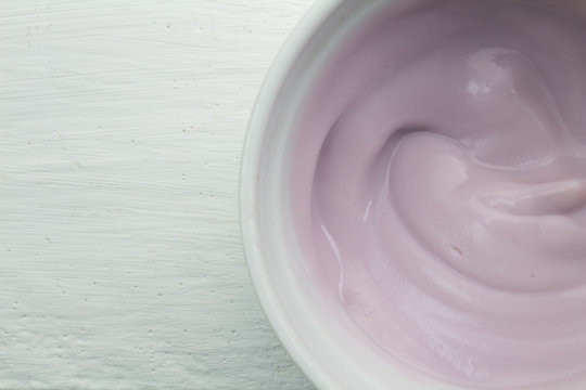 Creamy naturally colored rasberry fruit yogurt in white glass bowl on white wood table close up top view photograph
