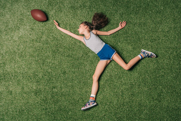 top view of little sportive girl catching rugby ball on grass, athletics children concept