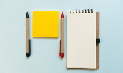Pens, yellow post note and blank notebook on blue background, view from above