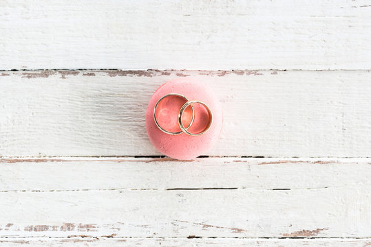 Top view of shiny golden wedding rings on pink macaron on wooden tabletop