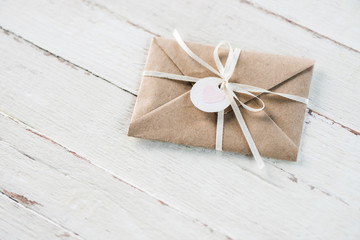 kraft envelope with teg with heart and ribbon on white wooden tabletop, invitation card wedding concept