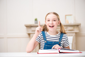 Adorable smiling girl reading book and pointing up with finger