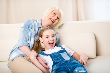 Happy grandmother and granddaughter having fun together on sofa