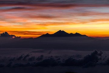 View of Rinjani peak from top of Agung volcano in Bali at sunrise summit. Sunrays and colorful sky, panoramic landscape, Agung trekking