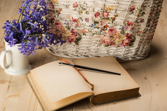 aged notebook with brush and lily flowers in a white cup and white basket - copy space