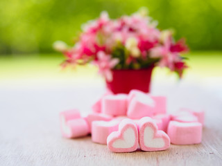 Closeup of sweet marshmallow in the shape of heart on wooden plate and flower at background. Concept about love and relationship. (Soft Style for Background)