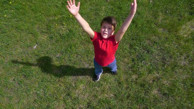 Boy throws up the ball, standing on green field, slow motion