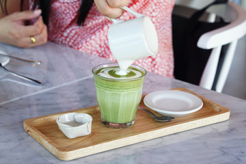A Woman's hand pouring steamed milk into a cup of Matcha green tea on the marble table, The traditional Chinese and Japanese tea.