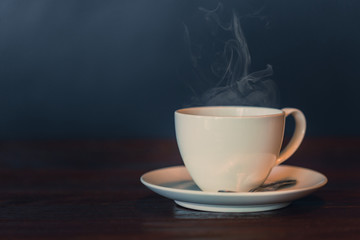 white hot coffee cup on wood table with smoke vapor on dark background vintage color tone.