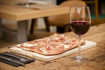 Traditional ham and brie cheese pizza with glass of red wine on rustic table