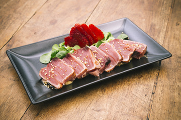Tuna tataki dish with stramberry, canon and sesame sauce on rustic wooden table