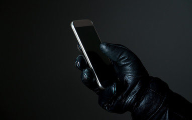 Mobile and cyber security threat concept. Criminal holding smartphone with black leather gloves in...