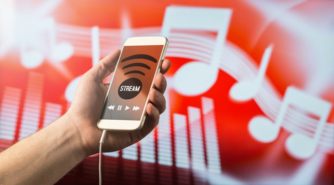 Close up of a man holding smartphone in hand and listening to music with mobile app. Red blurred note background. Modern online music streaming concept with free copy space for text.