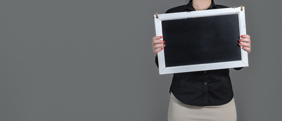 Woman holding chalkboard with copy space. Plenty of free blank room for text and content. Dark gray background. Girl with waitress or business style clothing showing empty blackboard.