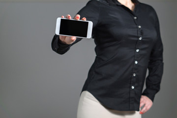 Business woman presenting a mobile application or showing a photo. Girl hold smartphone with dynamic pose and black collared shirt. Empty screen with copy space for text or content. Gray background.
