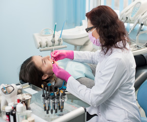 Female dentist with dental tools - mirror and probe checking up patient teeth at dental clinic...