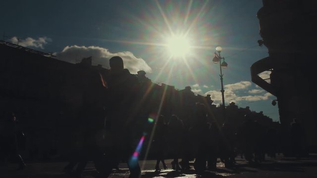 Crowd of anonymous people cross the roadway at the crossroads. Silhouettes of people walking on the street in conditions of heavy city traffic. Shooting from the lower angle against bright sun