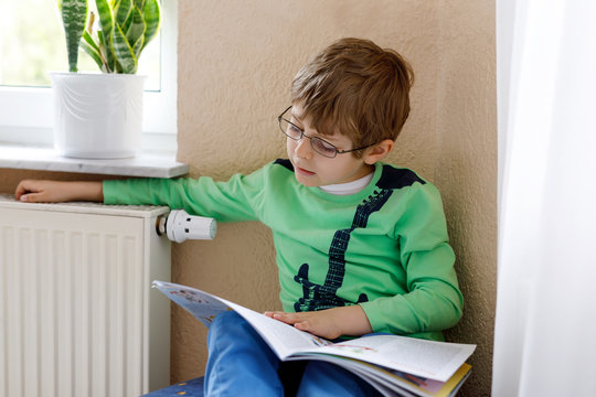 Little Blonde School Kid Boy With Glasses Reading A Book At Home