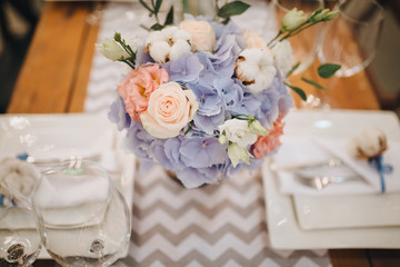 The wooden festive table is decorated with compositions of flowers, candles and served with cutlery, glasses and plates