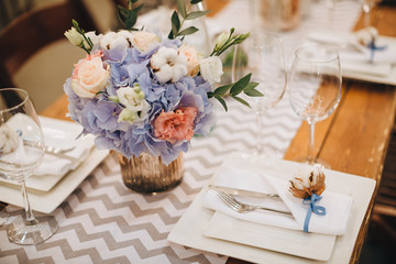 The wooden festive table is decorated with compositions of flowers, candles and served with cutlery, glasses and plates