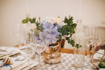 The wooden festive table is decorated with compositions of flowers, candles and served with cutlery, glasses and plates