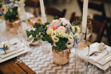 The wooden festive table is decorated with compositions of flowers, candles and served with cutlery, glasses and plates