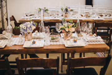 A wedding bouquet of bride stands on the table in the wedding banquet area, beside it there are candles and glass boxes with succulents