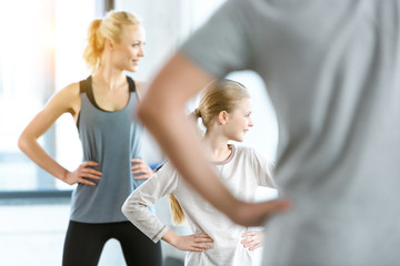 Young woman and cute girl exercising with coach at fitness studio