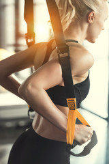 Blonde fitness woman training with trx fitness straps