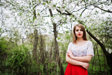 Portrait of beautiful girl with red lips at spring blossom garden, wear on red dress and white blouse.