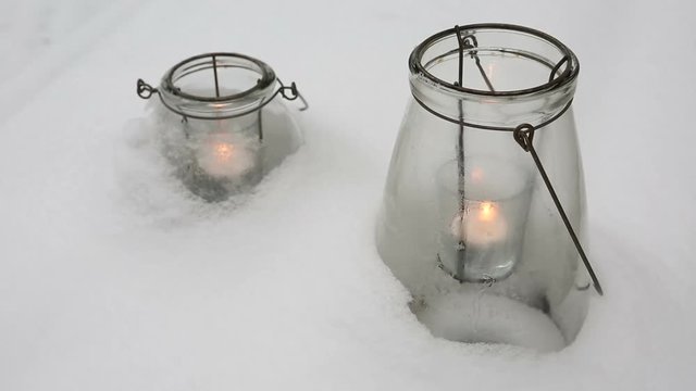 two candles in glasses in the snow
