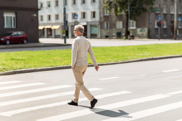 senior man walking along city crosswalk