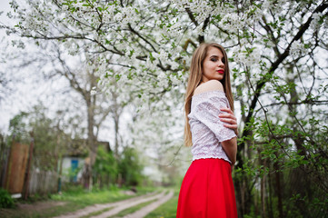 Fototapeta na wymiar Portrait of beautiful girl with red lips at spring blossom garden, wear on red dress and white blouse.
