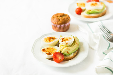 Healthy breakfast: toasts with avocado slices, tomato, paprika and eggs on white tableware. Selective focus