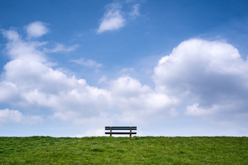 Einsame Bank mit grüner Wiese und Blick auf endlosen Himmel mit Wolken an einem Sommertag