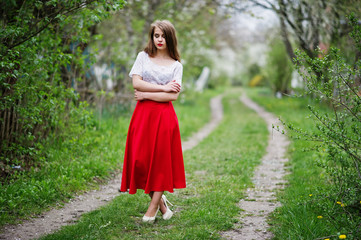 Obraz na płótnie Canvas Portrait of beautiful girl with red lips at spring blossom garden, wear on red dress and white blouse.