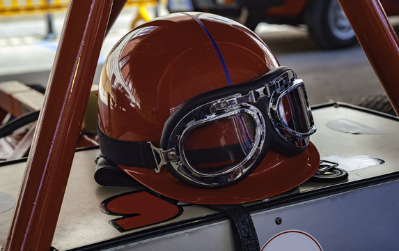 Vintage racing helmet and goggles sitting on the hood of a vintage sports car.