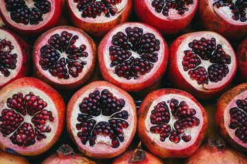 Rows of red juicy ripe sliced pomegranate on the market creating a background