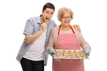 Young man tasting freshly baked cookie by his grandmother