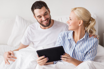 Fototapeta premium smiling happy couple with tablet pc in bed at home