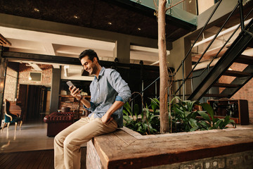 Happy young man in modern office lounge using mobile phone