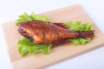 Smoked fish and lemon on green lettuce leaves on Wooden cutting board isolated on white background.