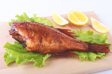 Smoked fish and lemon on green lettuce leaves on Wooden cutting board isolated on white background.