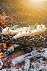 Grilled chicken fillets on a grill with spice and rosemary. Marinated chicken breast on flaming grill with vegetables. Healthy food. BBQ sauce. 