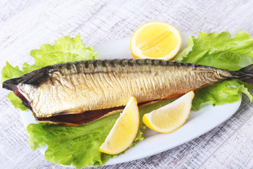 Smoked mackerele and lemon on green lettuce leaves on Wooden cutting board isolated on white background.