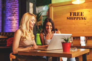 Two attractive women online via a laptop in a cafe
